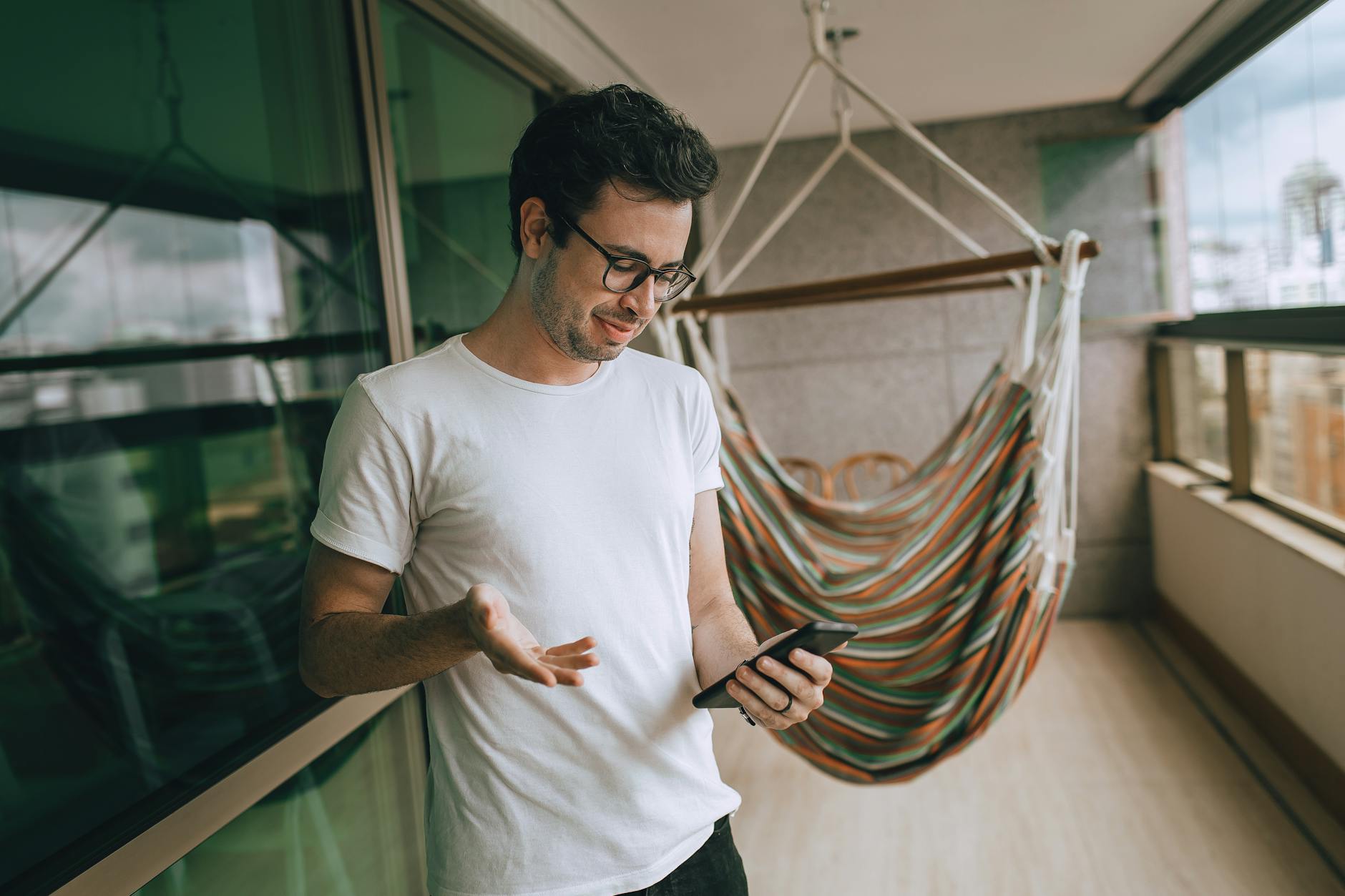 Adult man looking at a smartphone while standing in a bright room beside a hammock