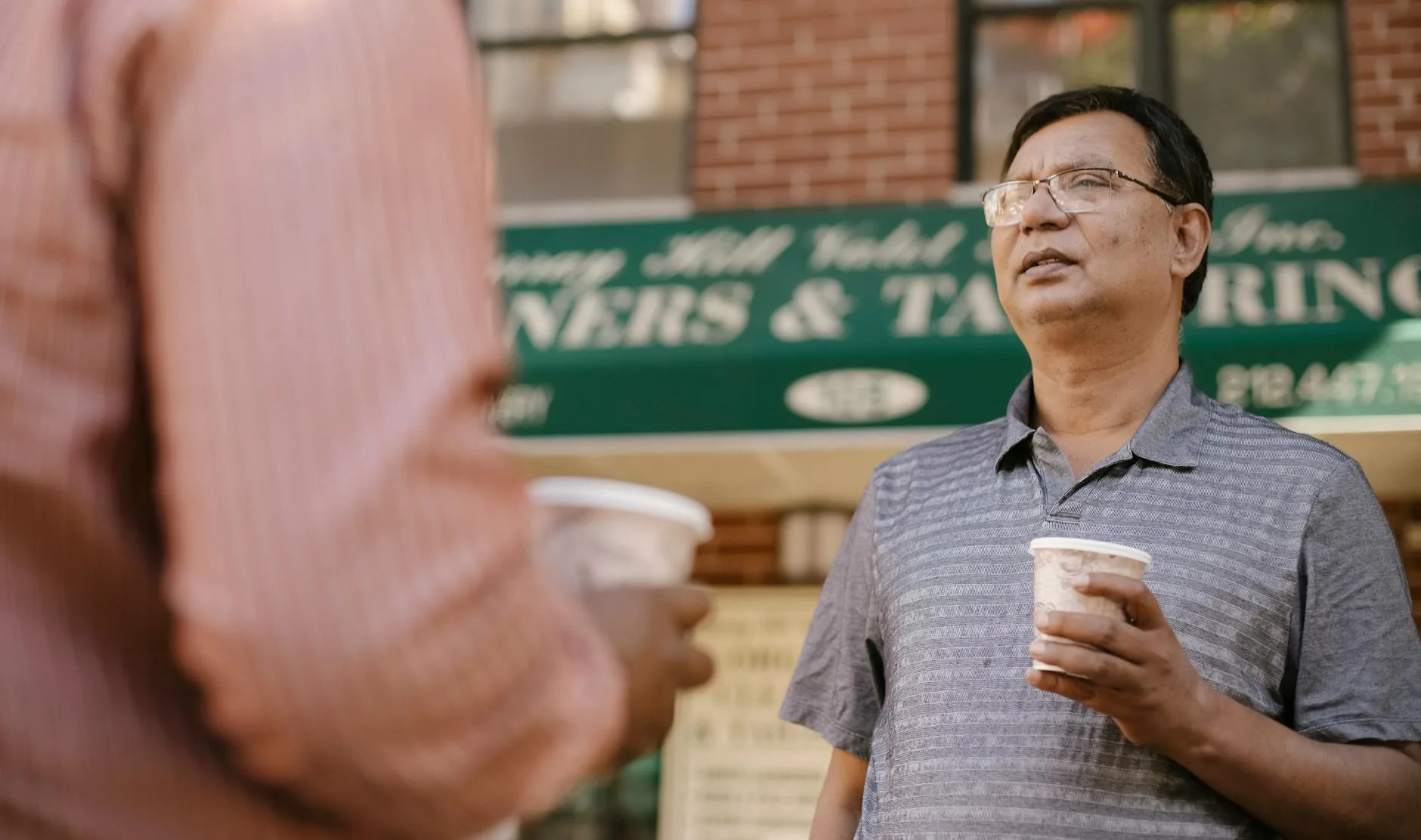 Two people holding takeaway cups while talking together.