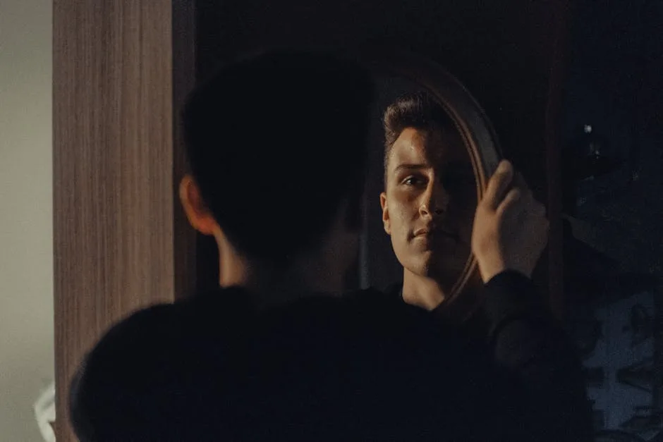 Young man holds a round mirror and looks at his reflection in a dim room.