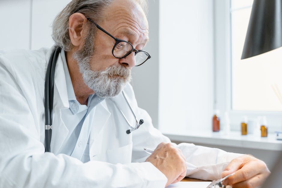 Elderly male doctor with glasses and stethoscope writing at a bright desk in a clinic.