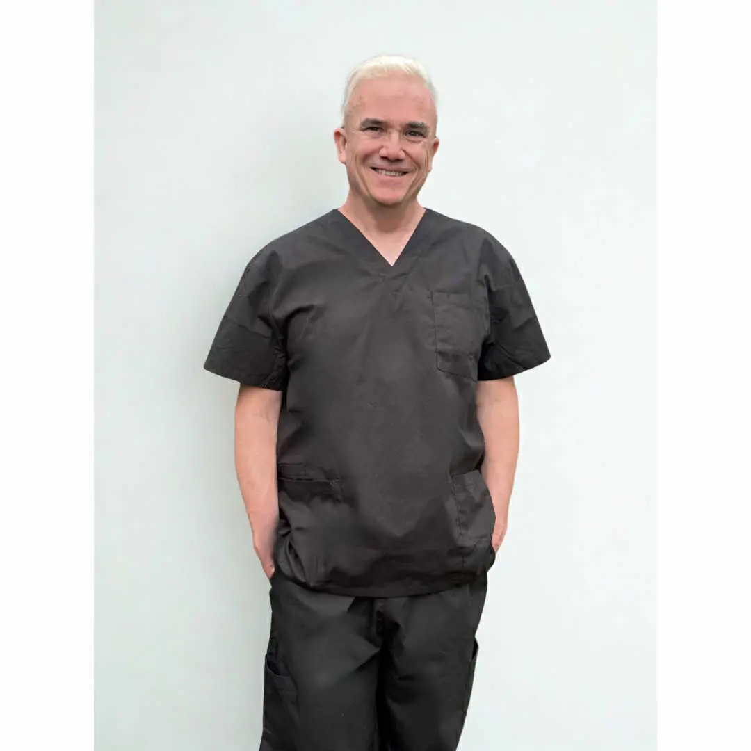 Corey Anderson smiling in black nursing scrubs against a plain wall